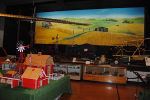 Inside the Minnesota Machinery Museum. A large mural of a wheat field. A small farm display which includes barns, windmill, and pasture. 