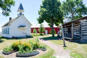 Outside the Lac qui Parle History Center. An old white church, flowers, and other historic buildings. 