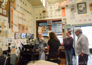 People visiting with a Meander artist in their studio. Studio walls are covered with prints. 