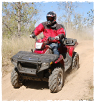 A person wearing a helmet and red coat driving a red for wheeler on a gravel path. 