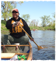 A man paddling a canoe down a calm river. 